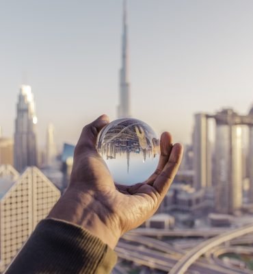 closeup-shot-male-hand-holding-crystal-ball-with-reflection-city-min